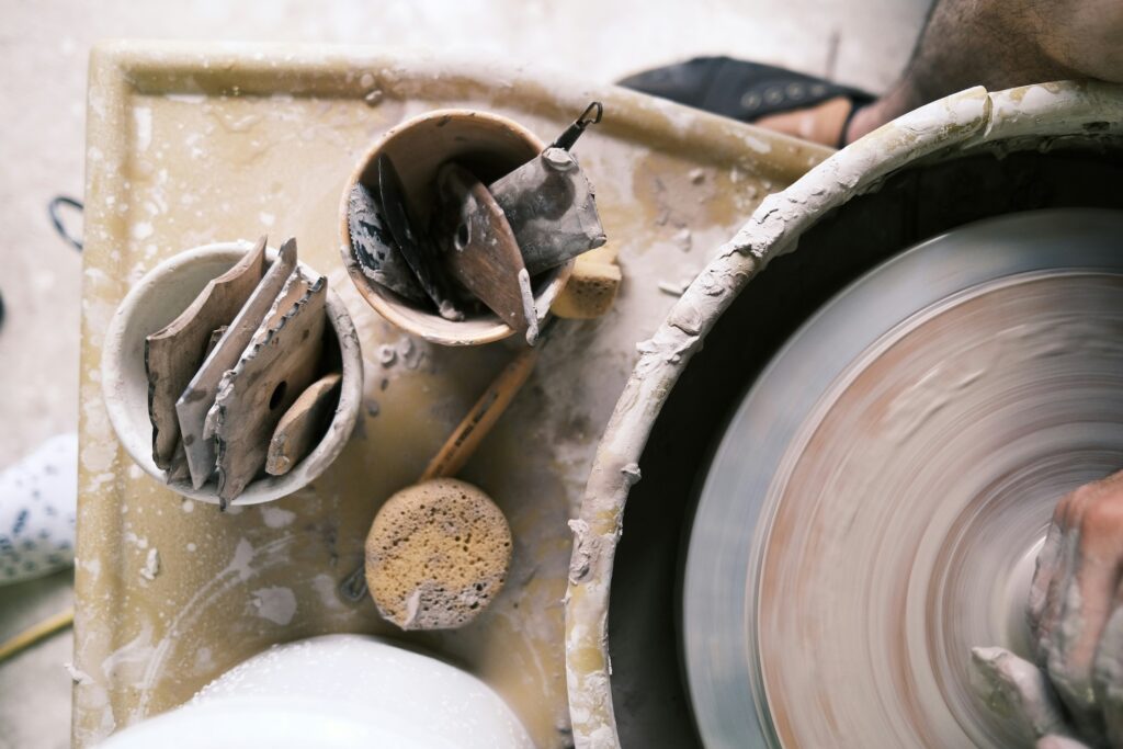 Closeup of potter's tools, with potter's hands and wheel visible at the edge of frame