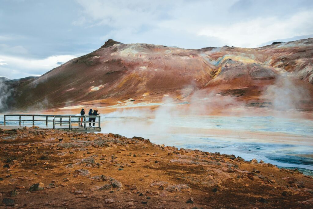 People look out across a steaming geothermal vent in Iceland