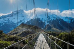 A suspension bridge stretches across a ravine with snow capped mountains in the background on a New Zealand Great Walk. 